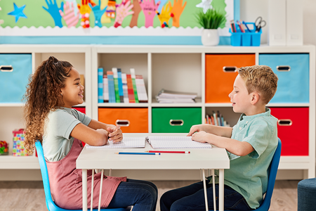 Children sitting at table across from eachother talking.